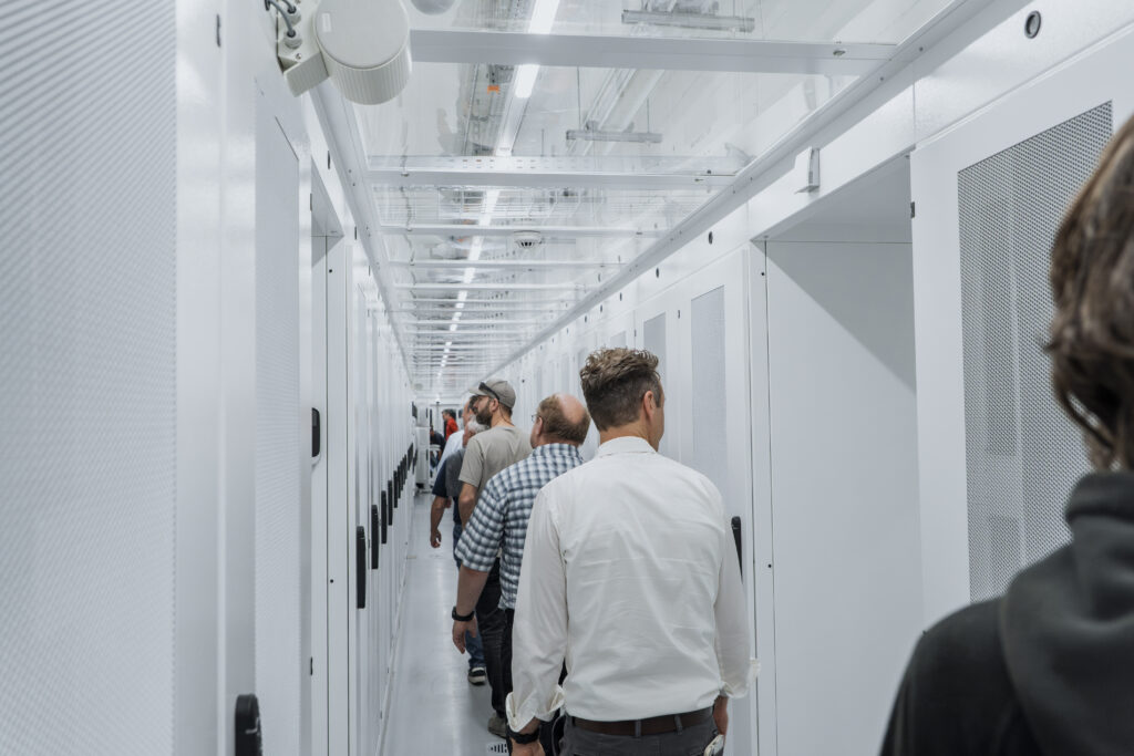Besuchergruppe in einem hellen Servergang des ARCON Datacenters in Luzern zwischen mehreren Reihen geschlossener Serverschränke.